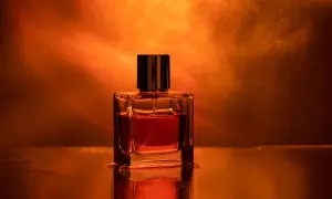 Szklana buteleczka perfum z bursztynowym płynem, otoczona ciepłym, pomarańczowym światłem. Zapach ambrowy unosi się w powietrzu.