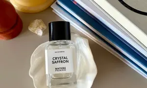 Elegancka butelka perfum "Crystal Saffron" na muszli, obok świecy i książek. Zapach orientalny, który przeniesie Cię w podróż.