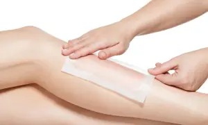 Dłonie przykładają plaster do depilacji na gładką skórę nogi. Dowiedz się, jak depilować nogi szybko i skutecznie.
