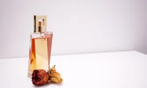 Elegancka butelka perfum z płynem w kolorze bursztynu, obok niej zasuszone róże. Wyobraź sobie, jak pozyskiwane jest piżmo, by stworzyć ten zapach.