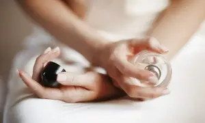 Dłonie kobiety trzymają flakonik perfum, gotowe do aplikacji. To jej osobisty kod perfum, który podkreśla jej styl.