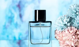 Elegancka butelka perfum lataffa z czarną nakrętką, obok pastelowych kwiatów.