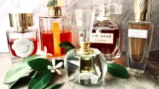 Kolekcja perfum z nutą **orange blossom**. Eleganckie flakony, wśród nich zapach Elie Saab, otoczone zielonymi liśćmi i białymi kwiatami.
