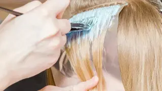 Fryzjerka nakłada rozjaśniacz na pasma włosów, przygotowując je do uzyskania efektu perłowy beż Loreal.