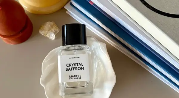 Elegancka butelka perfum "Crystal Saffron" na muszli, obok świecy i książek. Zapach orientalny, który przeniesie Cię w podróż.