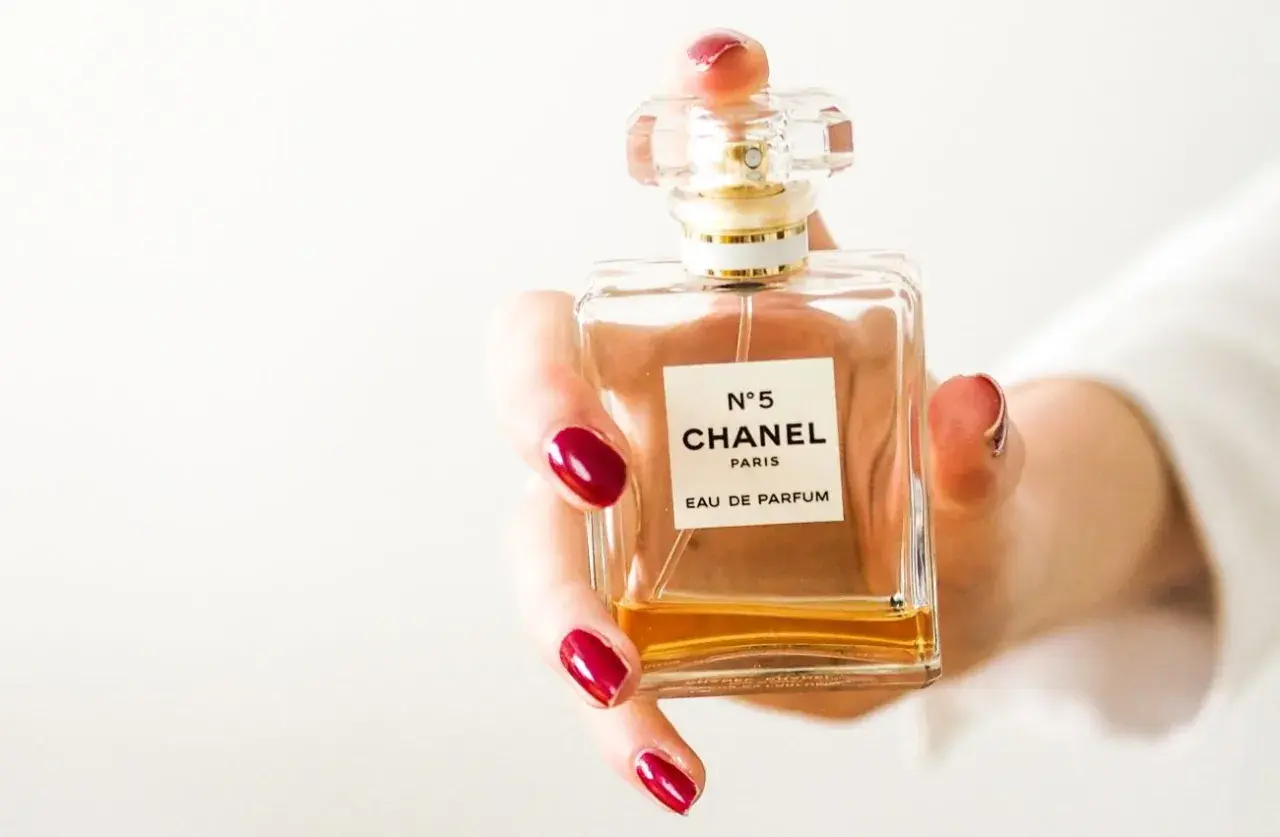 Dłoń z czerwonymi paznokciami trzyma flakonik Chanel N°5. Czy perfumy mogą się przeterminować? Ten klasyk pachnie wiecznie.