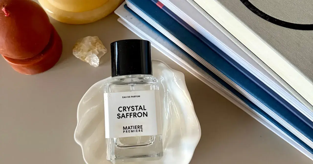 Elegancka butelka perfum "Crystal Saffron" na muszli, obok świecy i książek. Zapach orientalny, który przeniesie Cię w podróż.