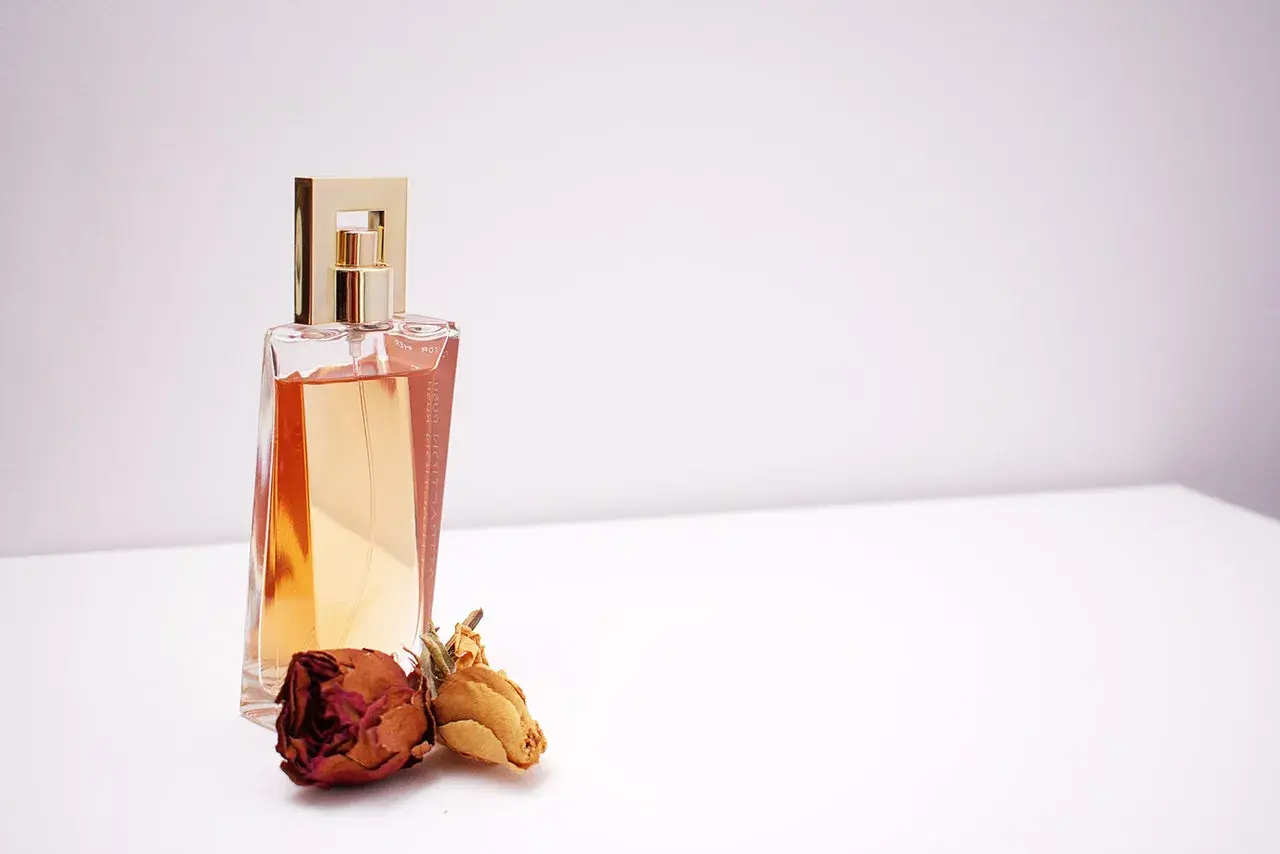 Elegancka butelka perfum z płynem w kolorze bursztynu, obok niej zasuszone róże. Wyobraź sobie, jak pozyskiwane jest piżmo, by stworzyć ten zapach.