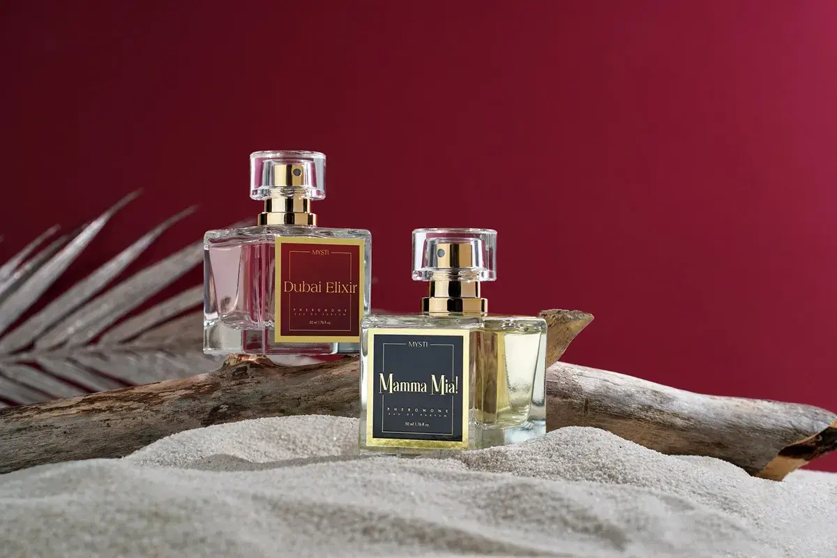 Dwa flakoniki perfum z feromonami, "Dubai Elixir" i "Mamma Mia!", na piasku i drewnie. Czy perfumy z feromonami działają?