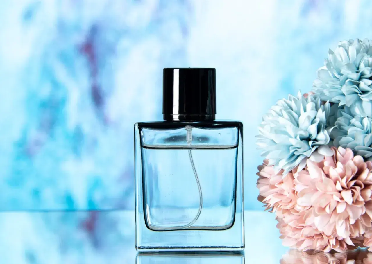 Elegancka butelka perfum lataffa z czarną nakrętką, obok pastelowych kwiatów.