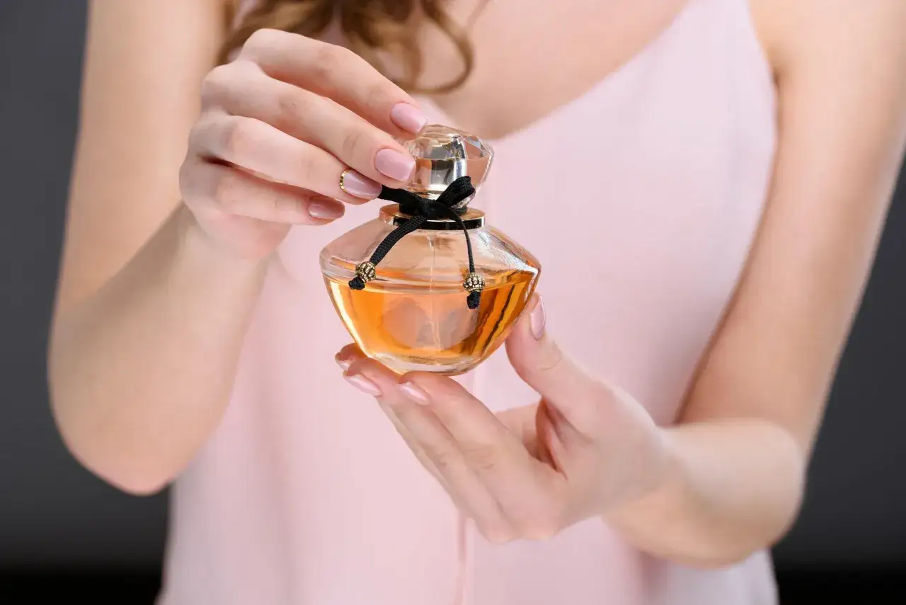 Dłonie kobiety trzymają buteleczkę z płynem, który może być najbardziej zmysłowe perfumy damskie. Elegancka wstążka zdobi flakon.