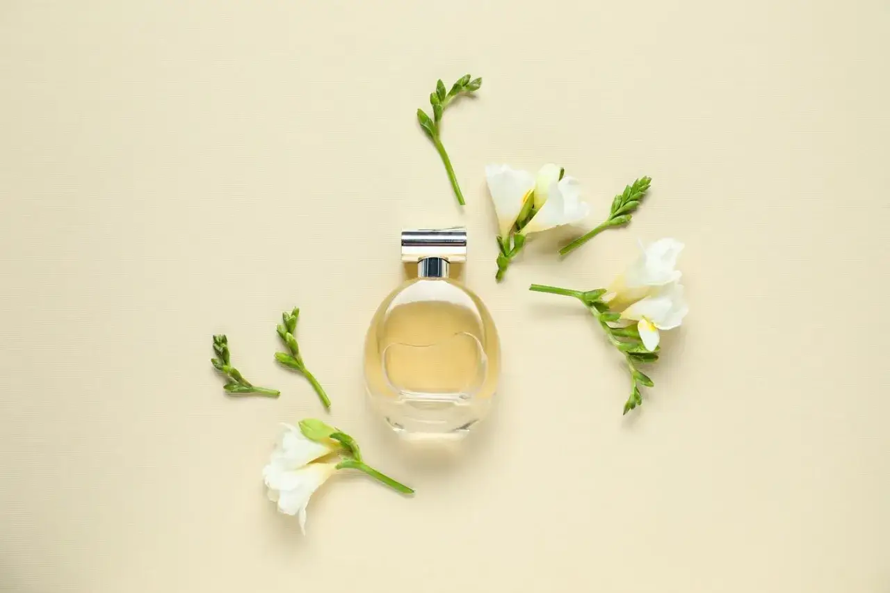 Elegancka butelka perfum otoczona białymi frezjami. Delikatny zapach frezji unosi się w powietrzu, tworząc subtelną kompozycję.